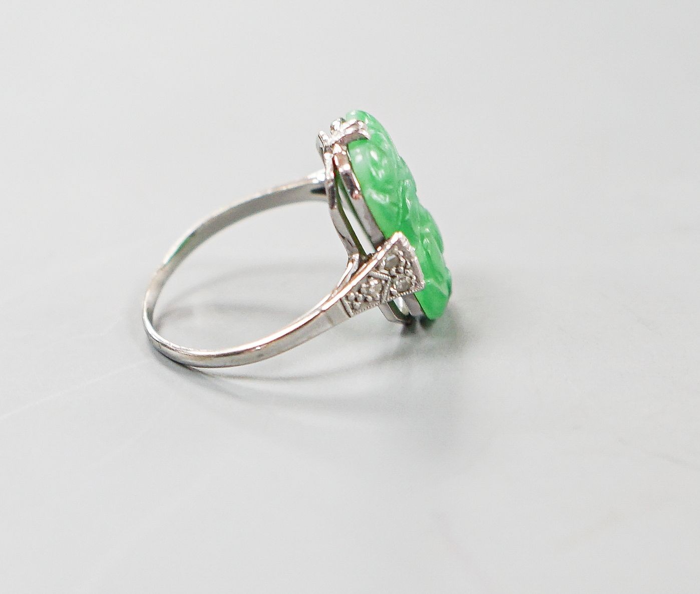 A 1920's 18ct, plat and carved jadeite oval dress ring, size O, gross weight 3.8 grams.